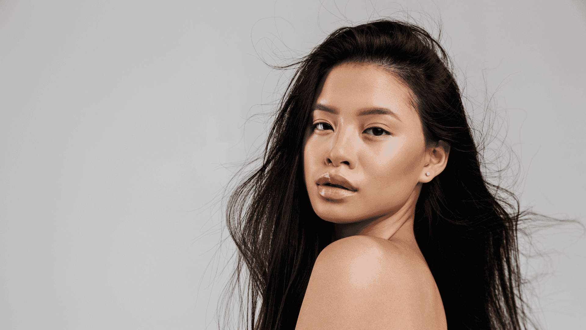 Young woman with long black hair gazing at camera, neutral background.