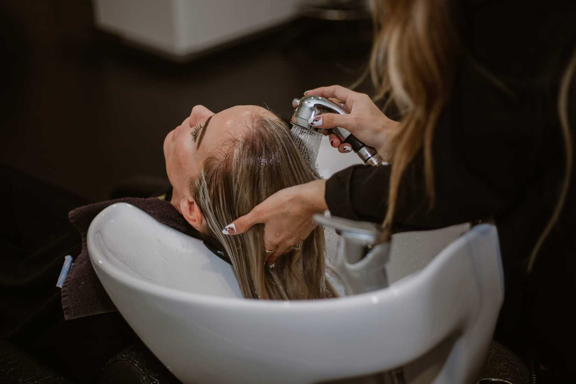 Hair stylist washing a client's hair in a salon sink.